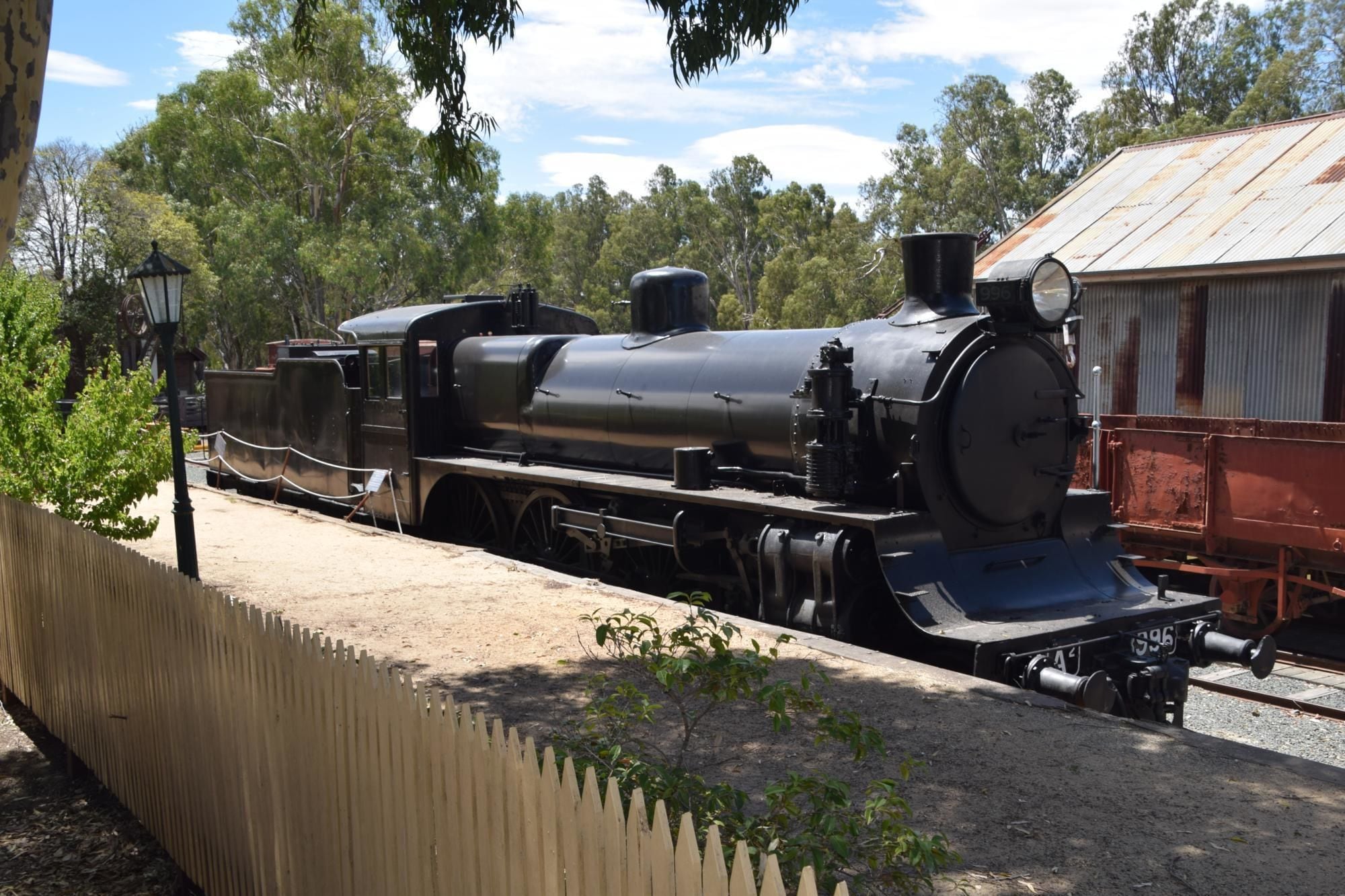 A steam locomotive on display, surrounded by a fence and trees.