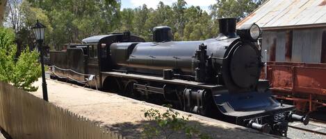 A steam locomotive on display, surrounded by a fence and trees.