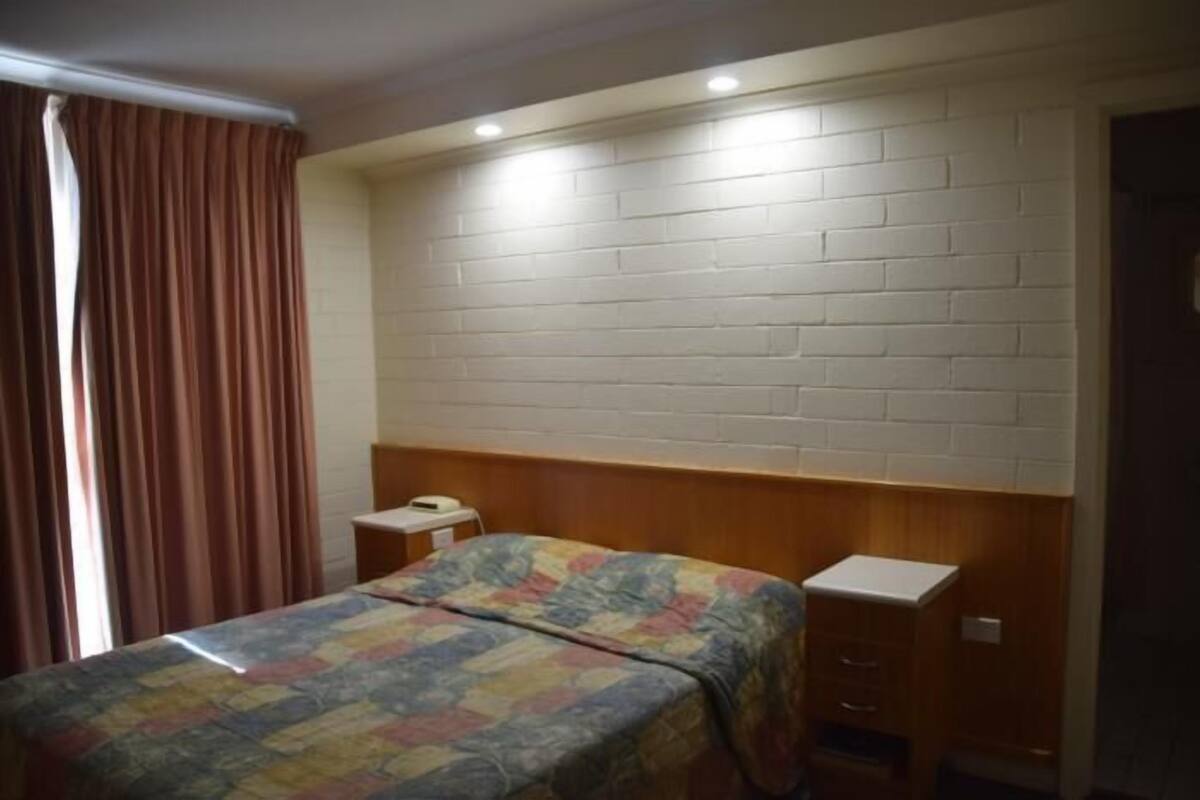A bedroom with a brick-patterned headboard, a bed with a colorful quilt, a bedside table, and a small wooden cabinet.