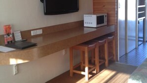 A modern kitchen with a flat-screen TV, a microwave, and wooden bar stools. - Big River Motel (Echuca)