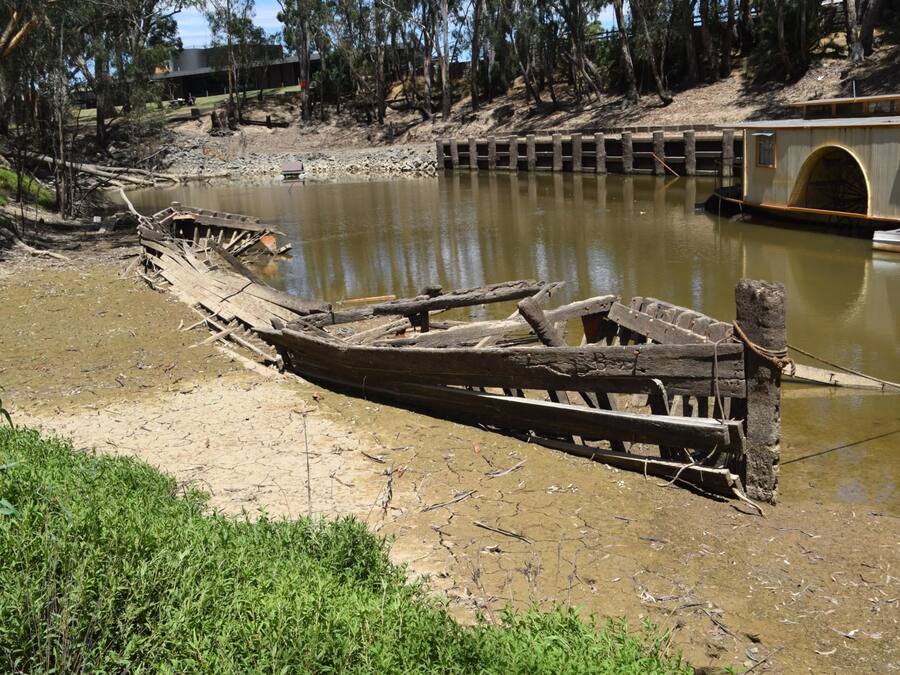 Ein hölzernes Boot am Flussufer, eine Betonbrücke und ein Gebäude mit einem gebogenen Eingang.