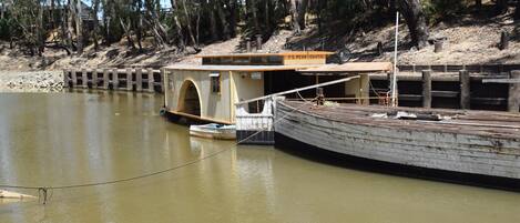 A houseboat docked at a river with a wooden deck and a small boat in front.