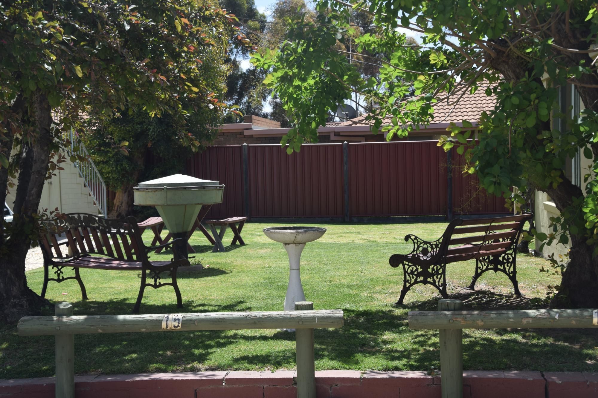 Un patio trasero con una parrilla, dos bancos, un bebedero para pájaros y un área cercada.