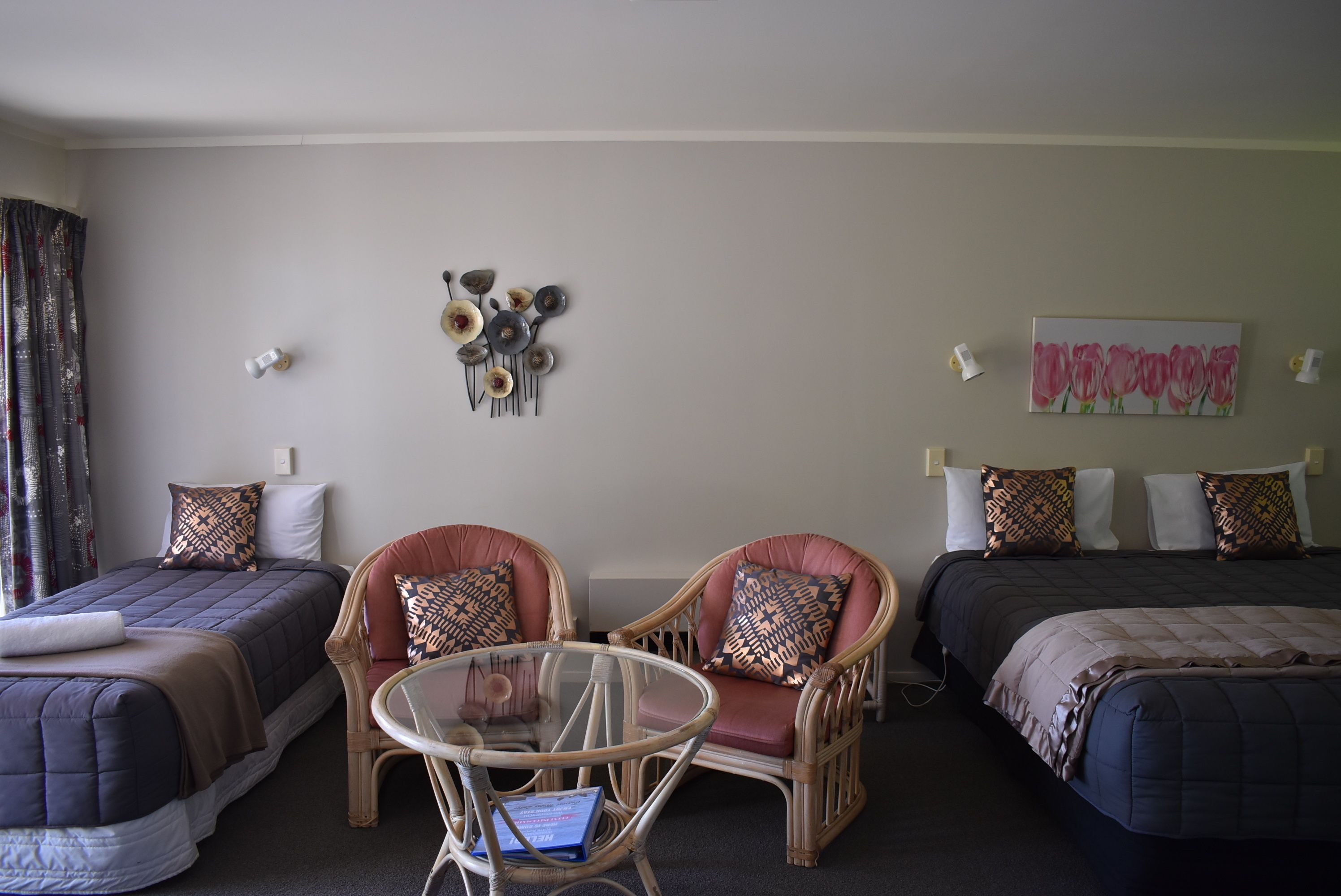 Een hotelkamer met twee eenpersoonsbedden, een zithoek met een glazen tafel en een decoratief wandobject.
