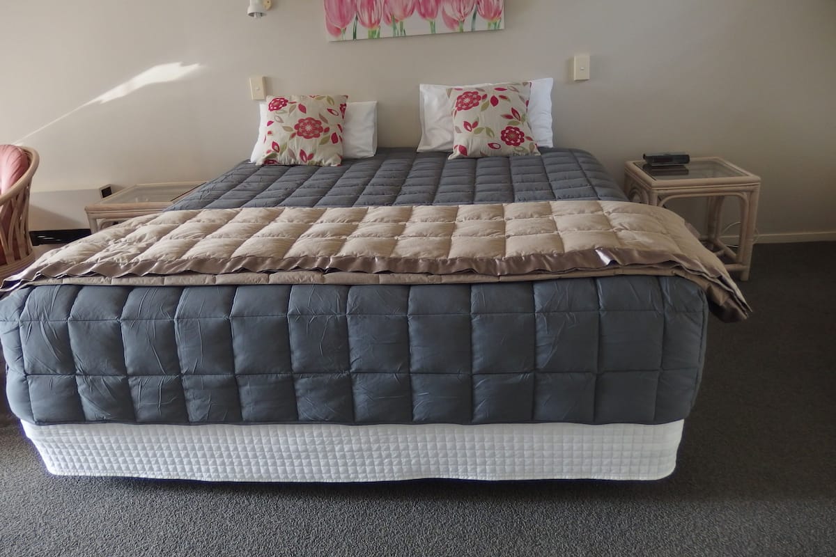 A bedroom with a large bed, two pillows, a bedside table, a chair, and a wall-mounted light fixture.