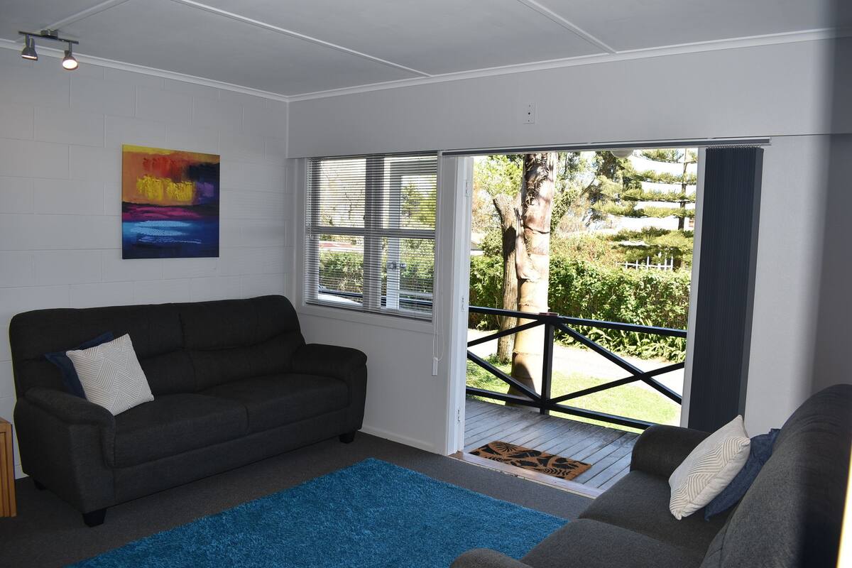 A living room with a dark sofa, a blue rug, and a colorful abstract painting on the wall.