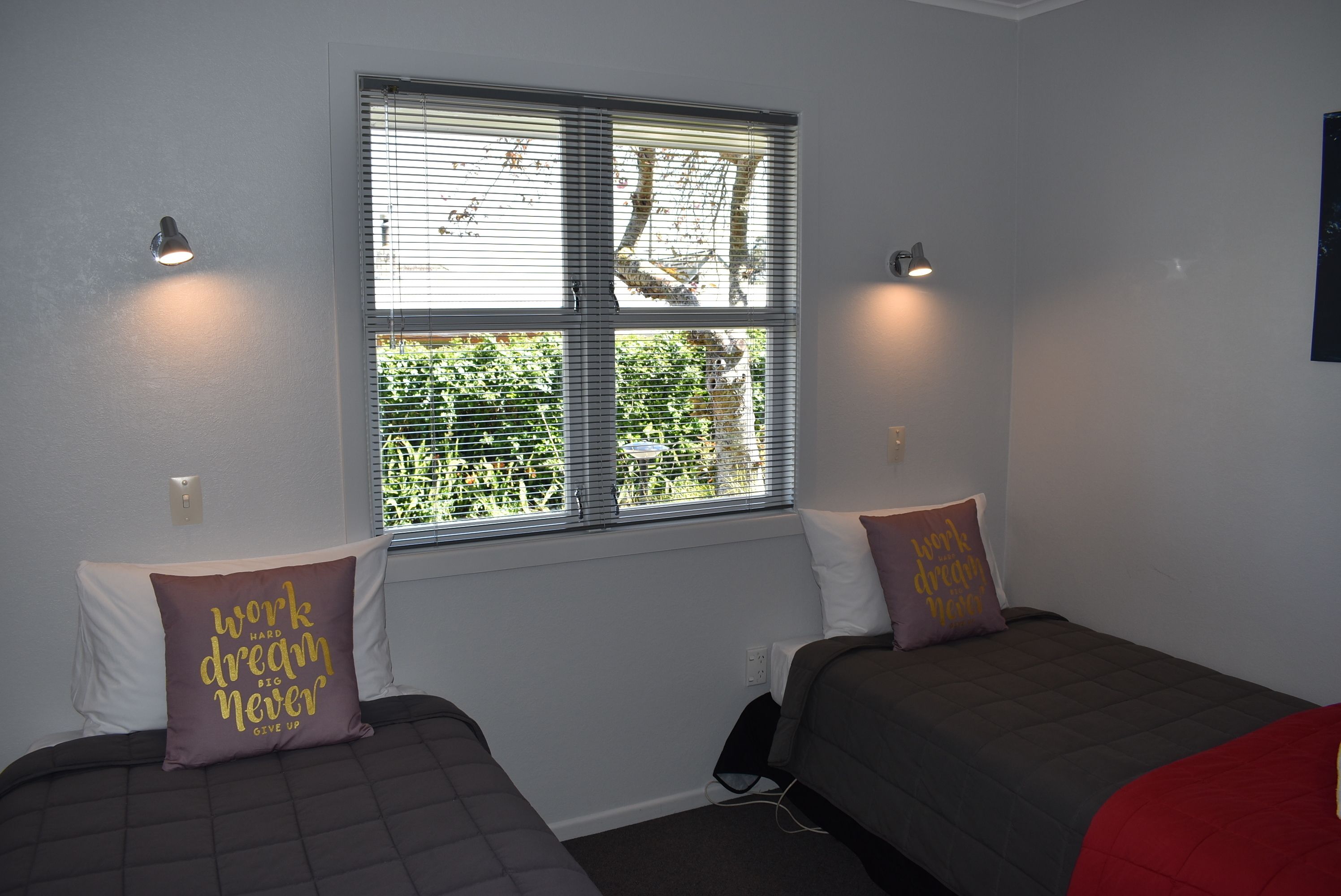 Een kamer met twee bedden, elk voorzien van een kussen, een raam met zonwering en wandlampen.