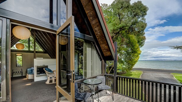 A modern outdoor deck with a glass door leading to a living area with a sofa and chairs, overlooking a body of water.