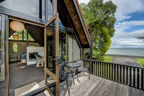 Una terraza moderna al aire libre con puerta de vidrio que da a un espacio de estar con sofá y sillones, con vista a una masa de agua.