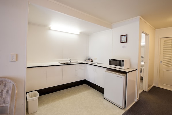 A compact kitchen with white cabinets, a microwave, a sink, and a trash bin.