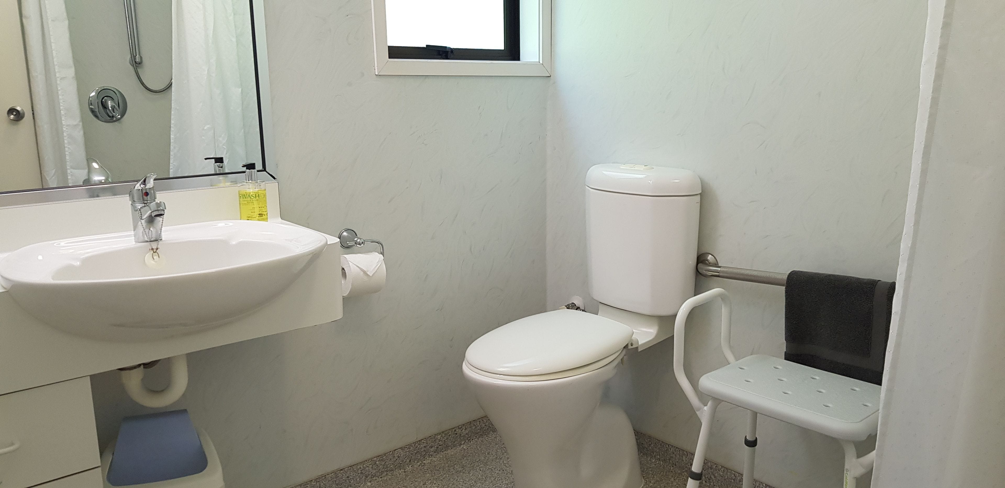 A bathroom with a white sink, toilet, and a small white chair.