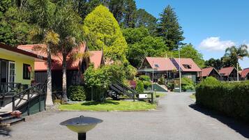A pathway leading to a building with a red roof, surrounded by greenery and a clear sky.