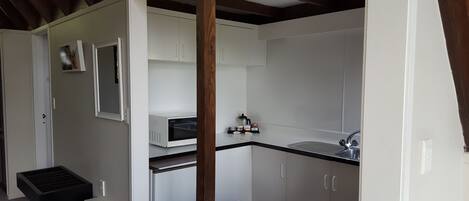 Une cuisine compacte avec des meubles blancs, un four à micro-ondes encastré, un évier et un plafond avec une poutre en bois.