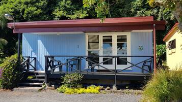 A small, single-story building with a blue exterior and a red roof. It features a porch with a railing and several chairs.