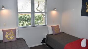 A room with two beds, each with a grey and red blanket, and a window with blinds.