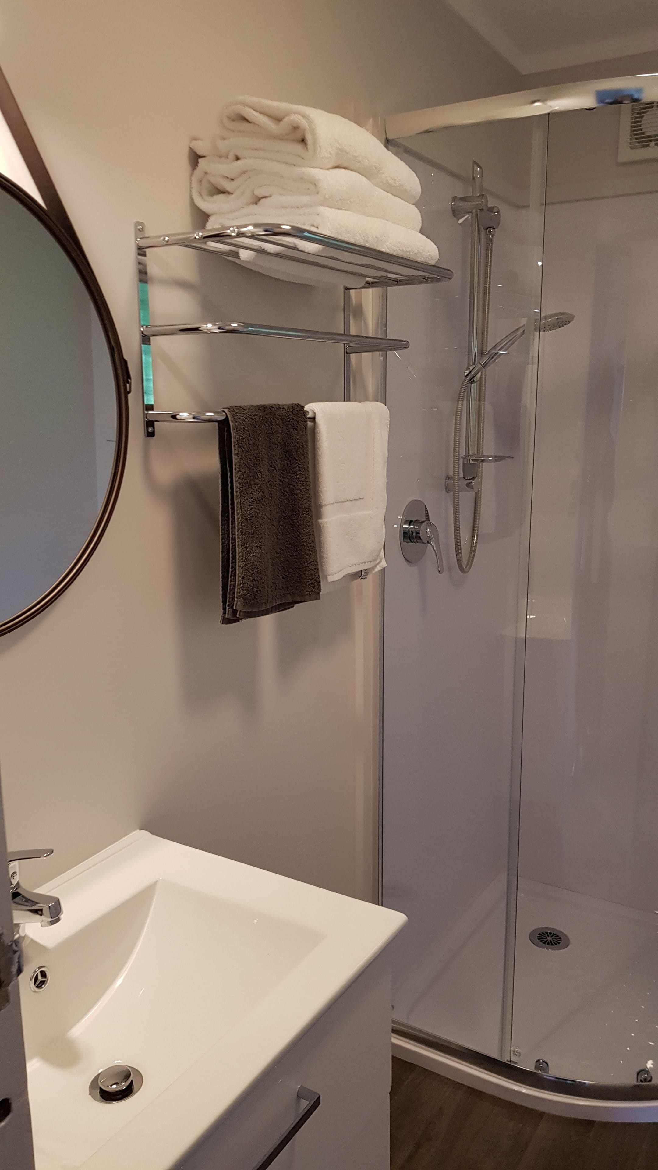 A bathroom with a white sink, a mirror, a towel rack with folded towels, and a glass-enclosed shower.