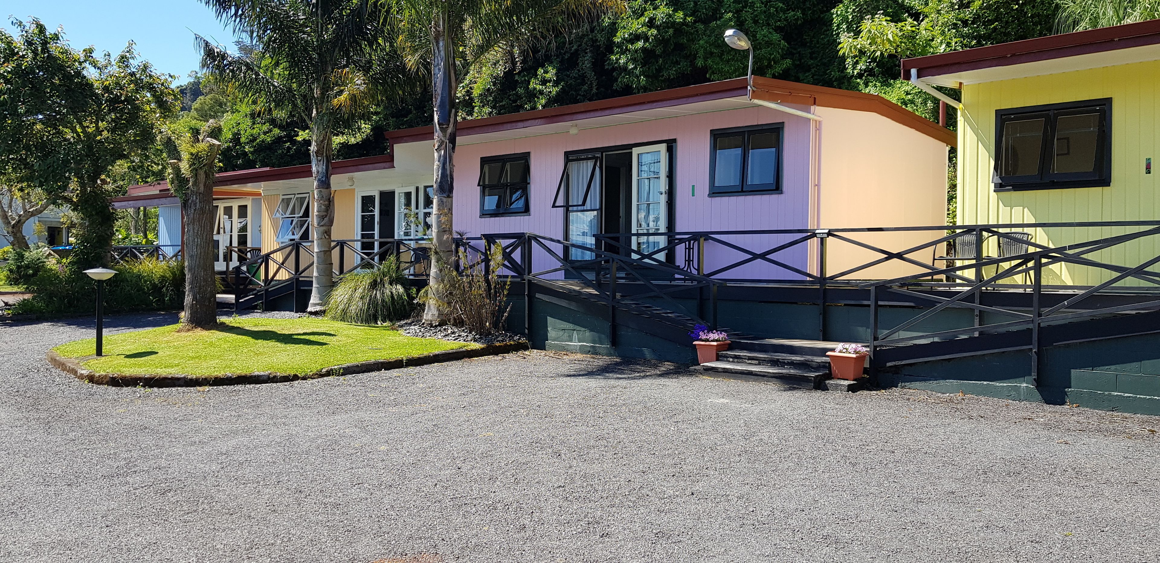 Une rangée de maisons mobiles aux couleurs vives, avec une allée en gravier et un petit espace jardin.
