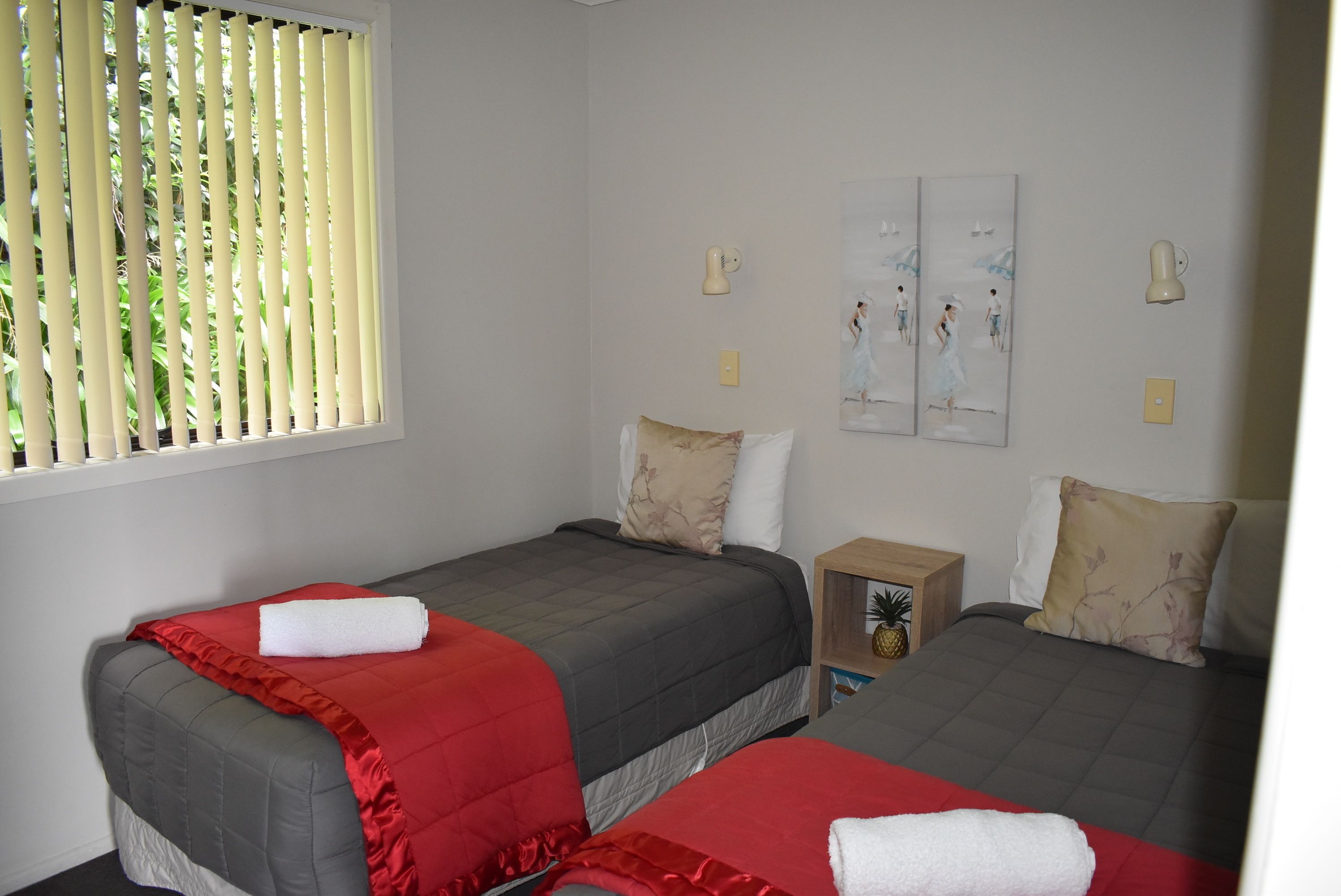 Ein Zimmer mit zwei Betten, jeweils mit einer roten und grauen Bettdecke, und einem kleinen Nachttisch mit einer Ananas-Dekoration.