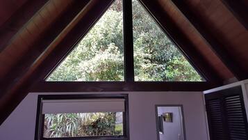 A room with a sloped ceiling, a window with a view of greenery, and a door with a light switch.