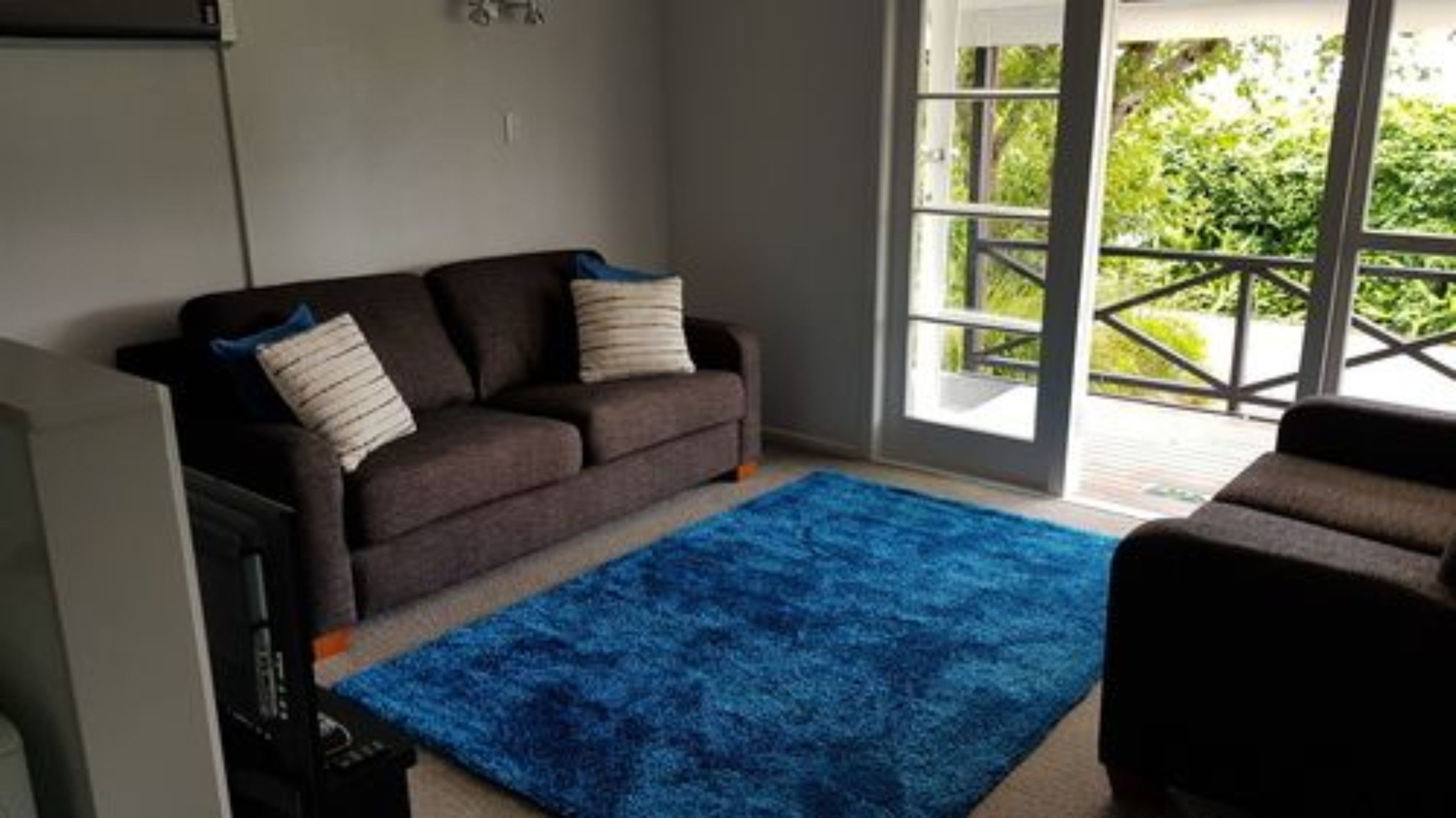 A living room with a dark brown sofa, two white cushions, a blue rug, and a television.