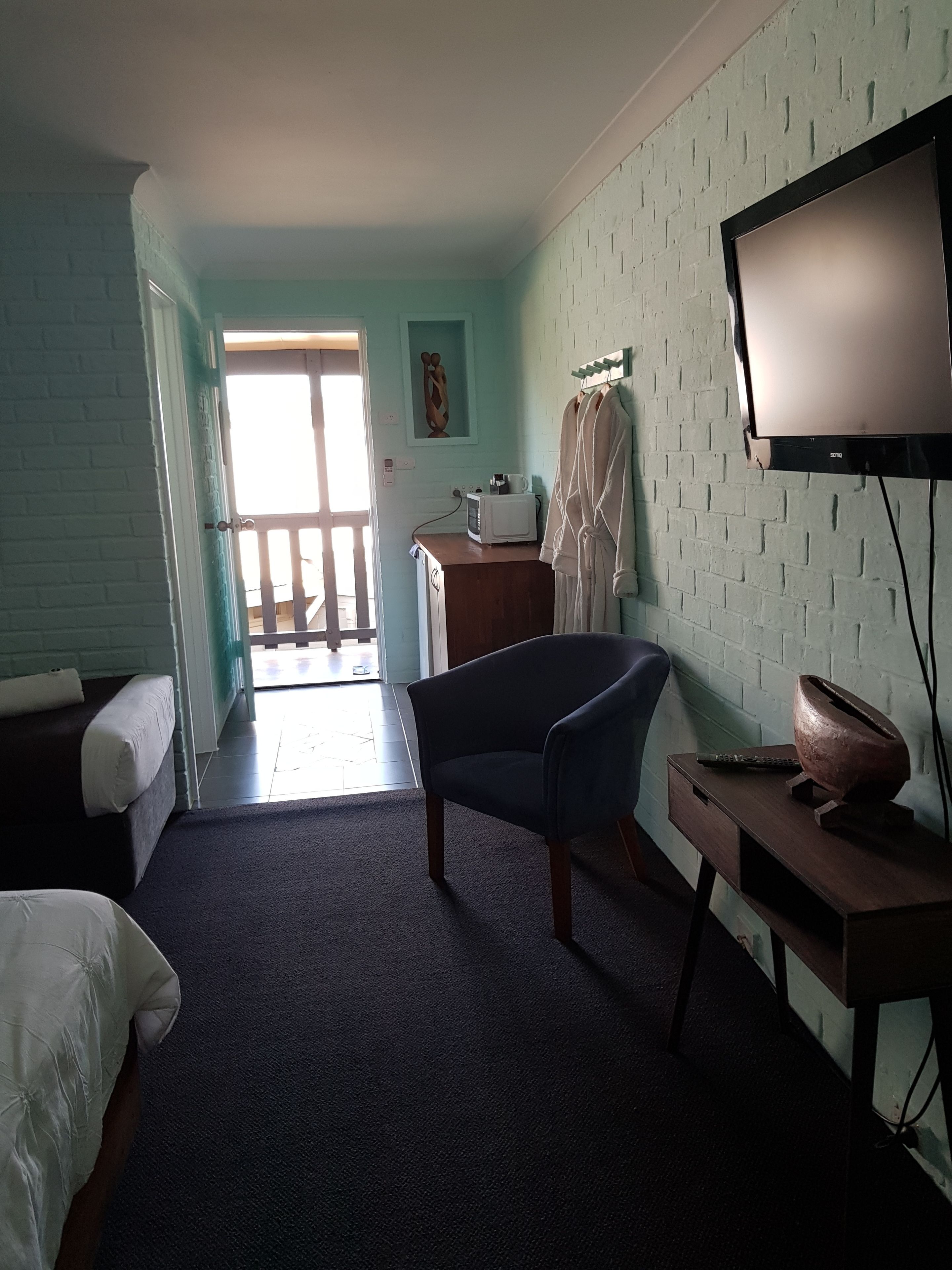 Una habitación con una cama, una silla, un escritorio con televisor, un microondas y un cuadro en la pared.