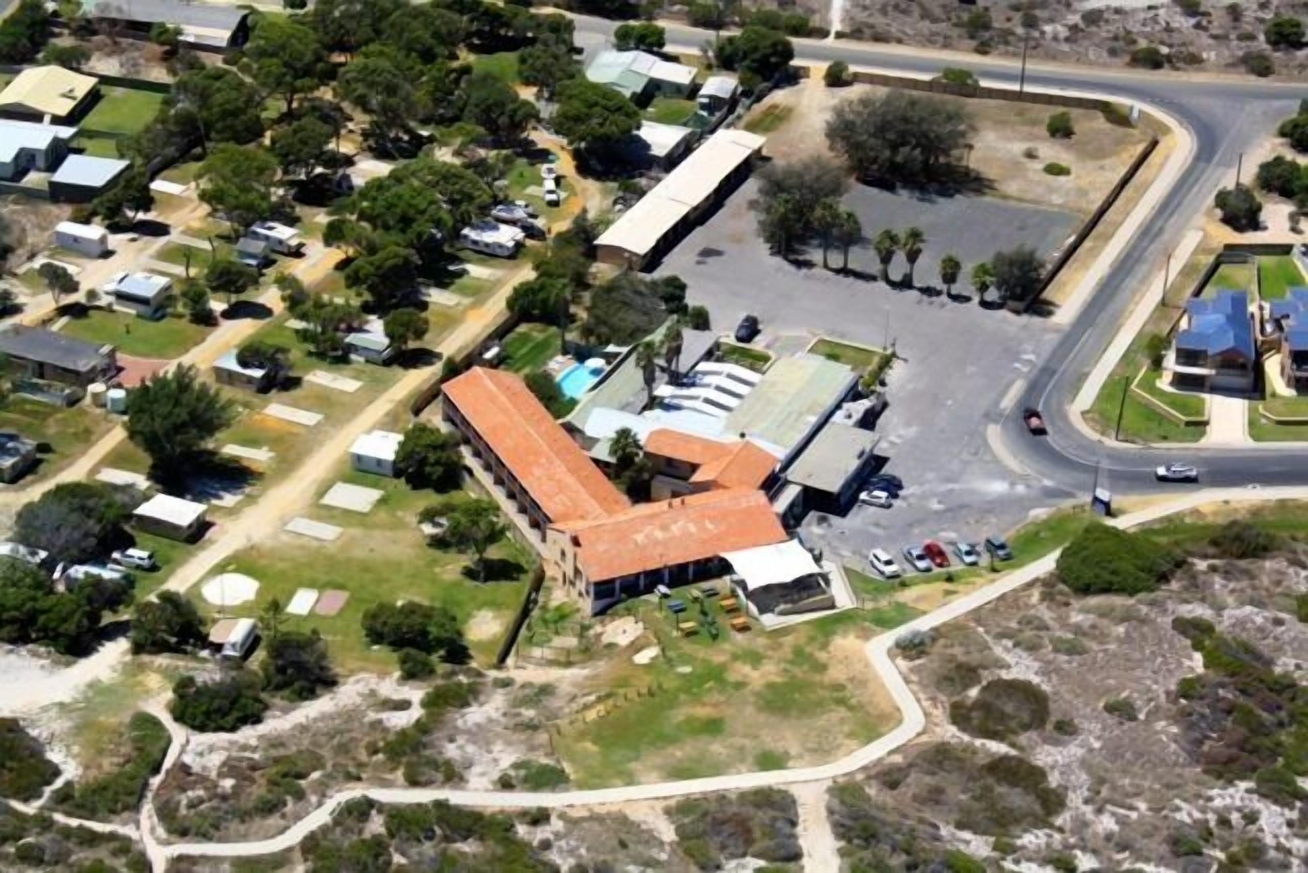 An aerial view of a residential area with a large building with a red roof, surrounded by parked cars and greenery.