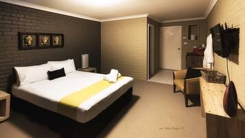 Habitación de hotel con cama, mesita de noche, silla, televisor y puerta.
