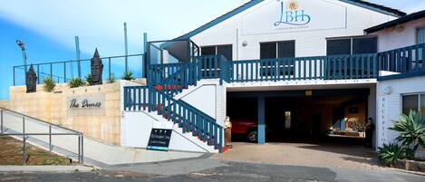 Un hôtel situé en bord de mer, doté d’un hall d’accueil, d’un escalier menant à l’entrée et d’une enseigne indiquant la présence d’un restaurant au rez-de-chaussée.