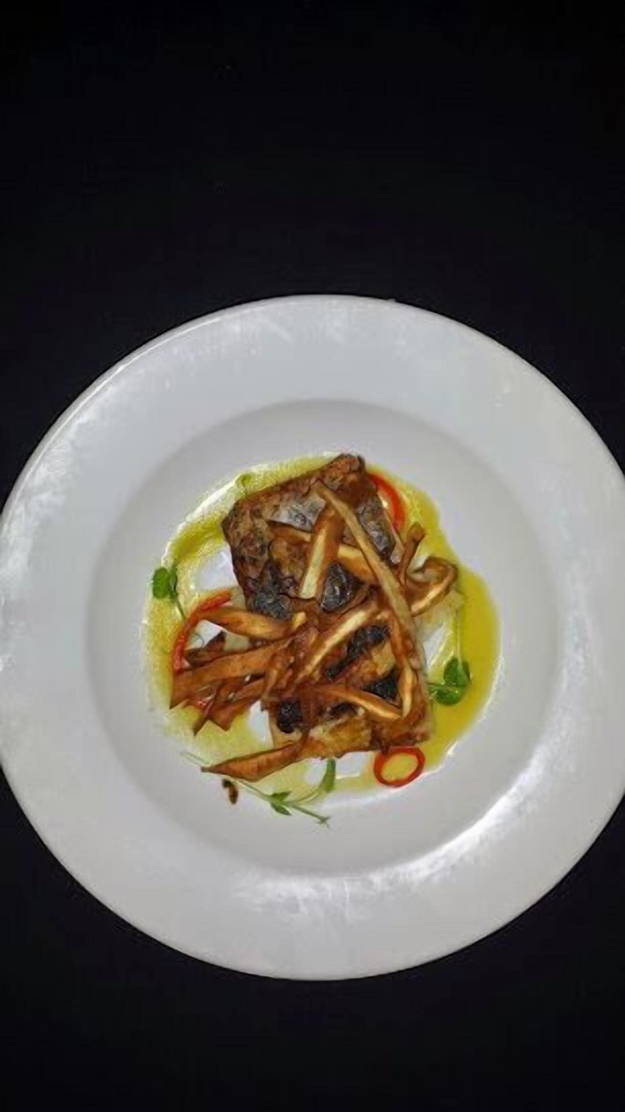 A white plate with a fish dish, possibly a fillet, accompanied by sautéed onions and garnished with herbs.