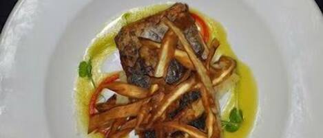 A white plate with a fish dish, possibly a fillet, accompanied by sautéed onions and garnished with herbs.