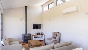 Een moderne woonkamer met een bank, fauteuils, een salontafel, een open haard en een tv aan de muur.