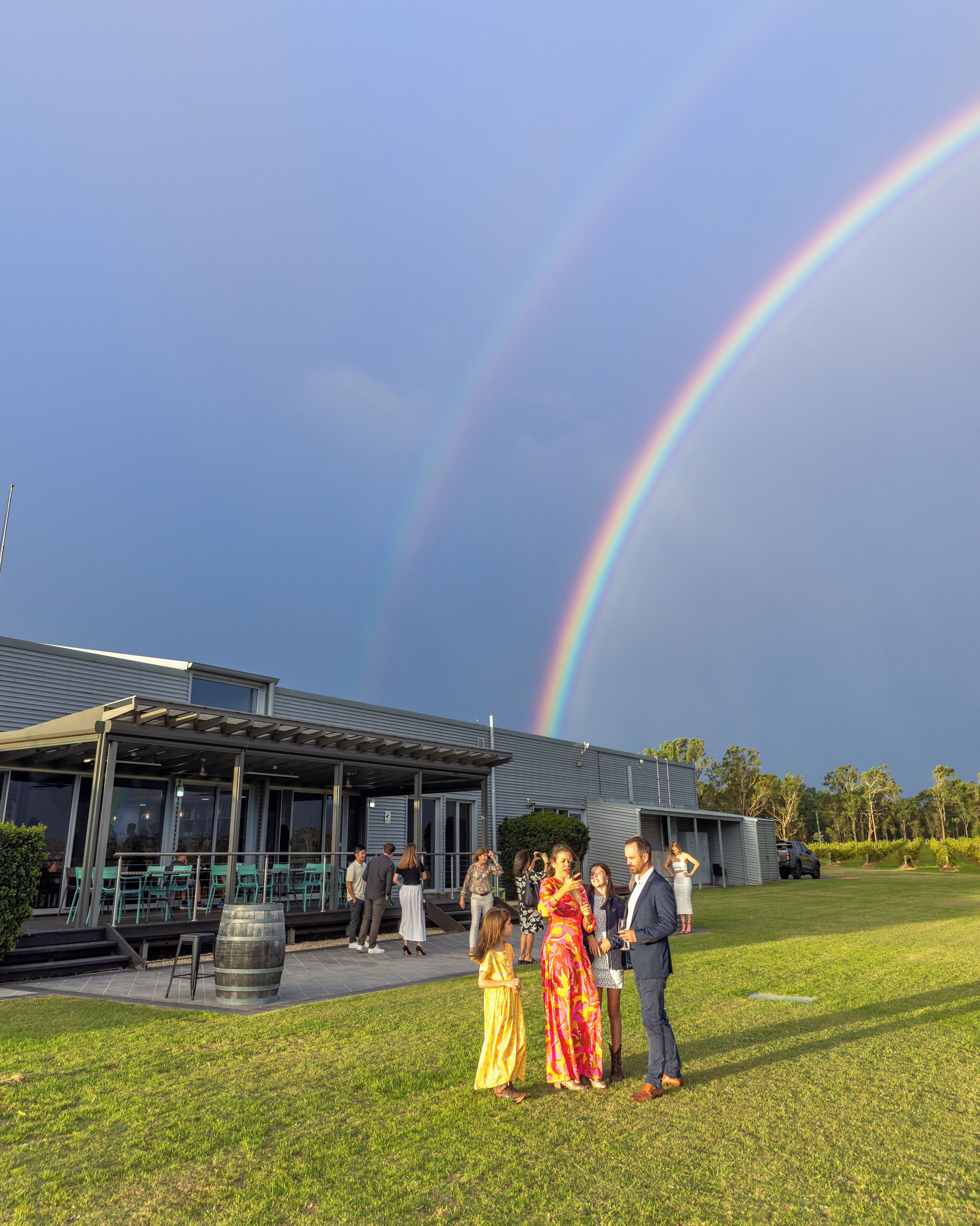 A building with a covered patio area, a grassy lawn, and a rainbow in the sky.