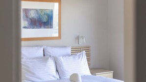 Een netjes opgemaakt bed met witte lakens, een rode plaid en een witte handdoek.