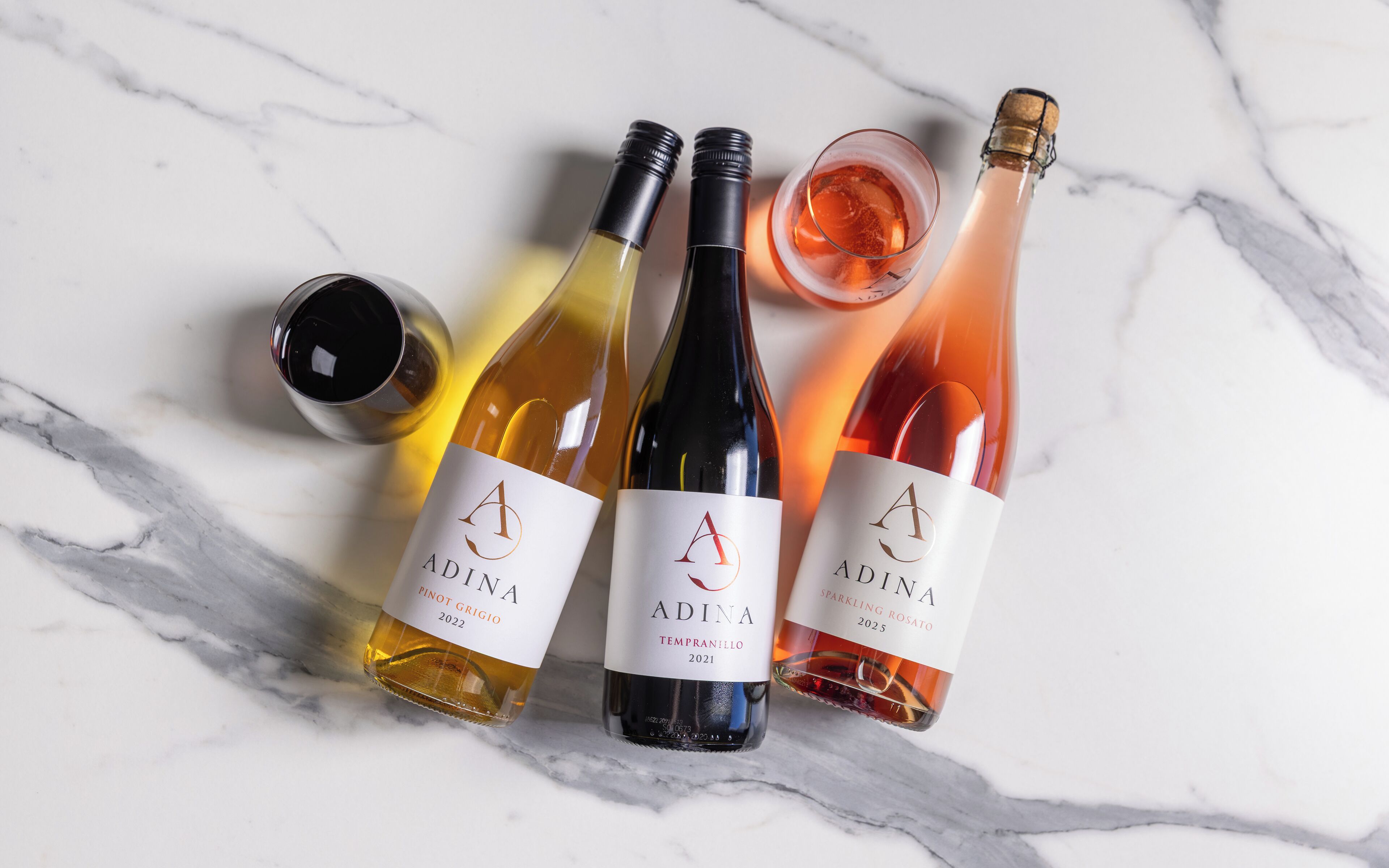 Tres botellas de vino Adina sobre una superficie de mármol.