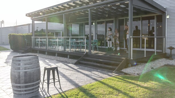 Een modern gebouw met een overdekt terras, een houten vat en een gazon.