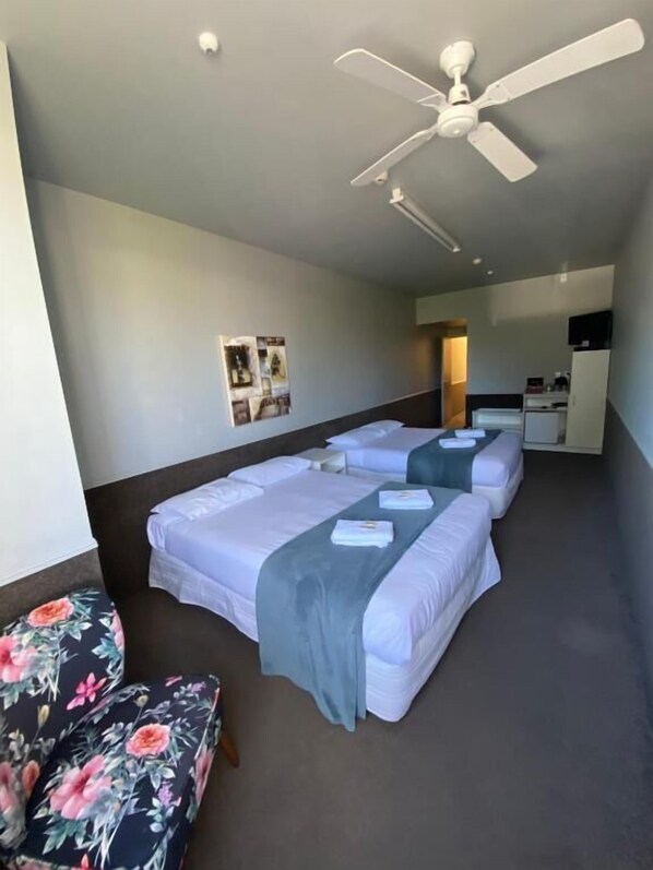 A hotel room with a bed, a desk, a chair, and a ceiling fan.