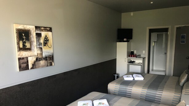 A hotel room with two beds, a TV on a stand, a small desk with a coffee maker, and a door leading to a bathroom.