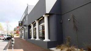 A modern building with a dark facade, white columns, and a brick-paved entrance.