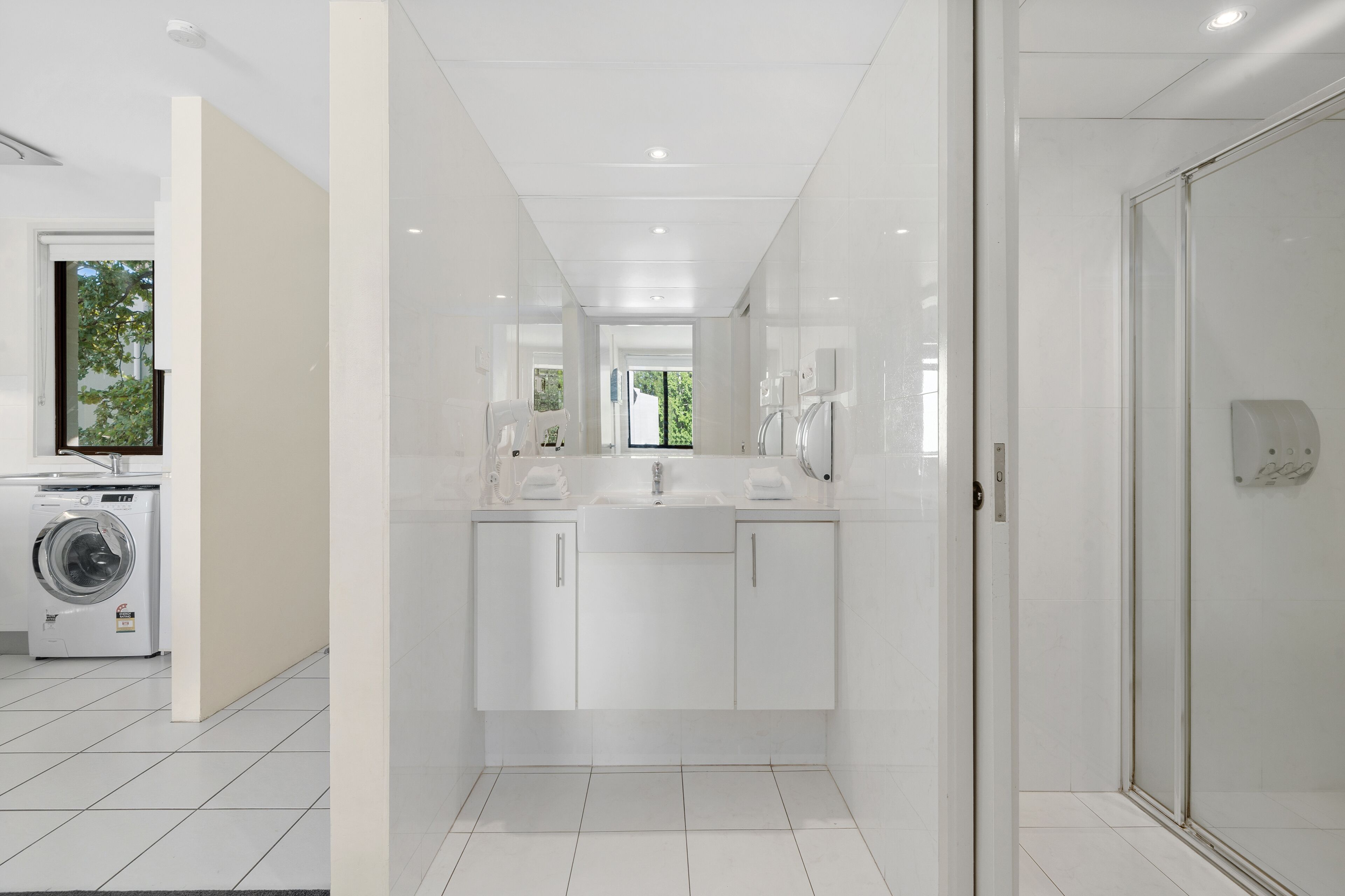 A modern bathroom with a built-in washing machine, a double sink vanity, and a glass shower enclosure.