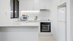 Una cocina moderna con armarios blancos, horno empotrado, microondas y refrigerador.