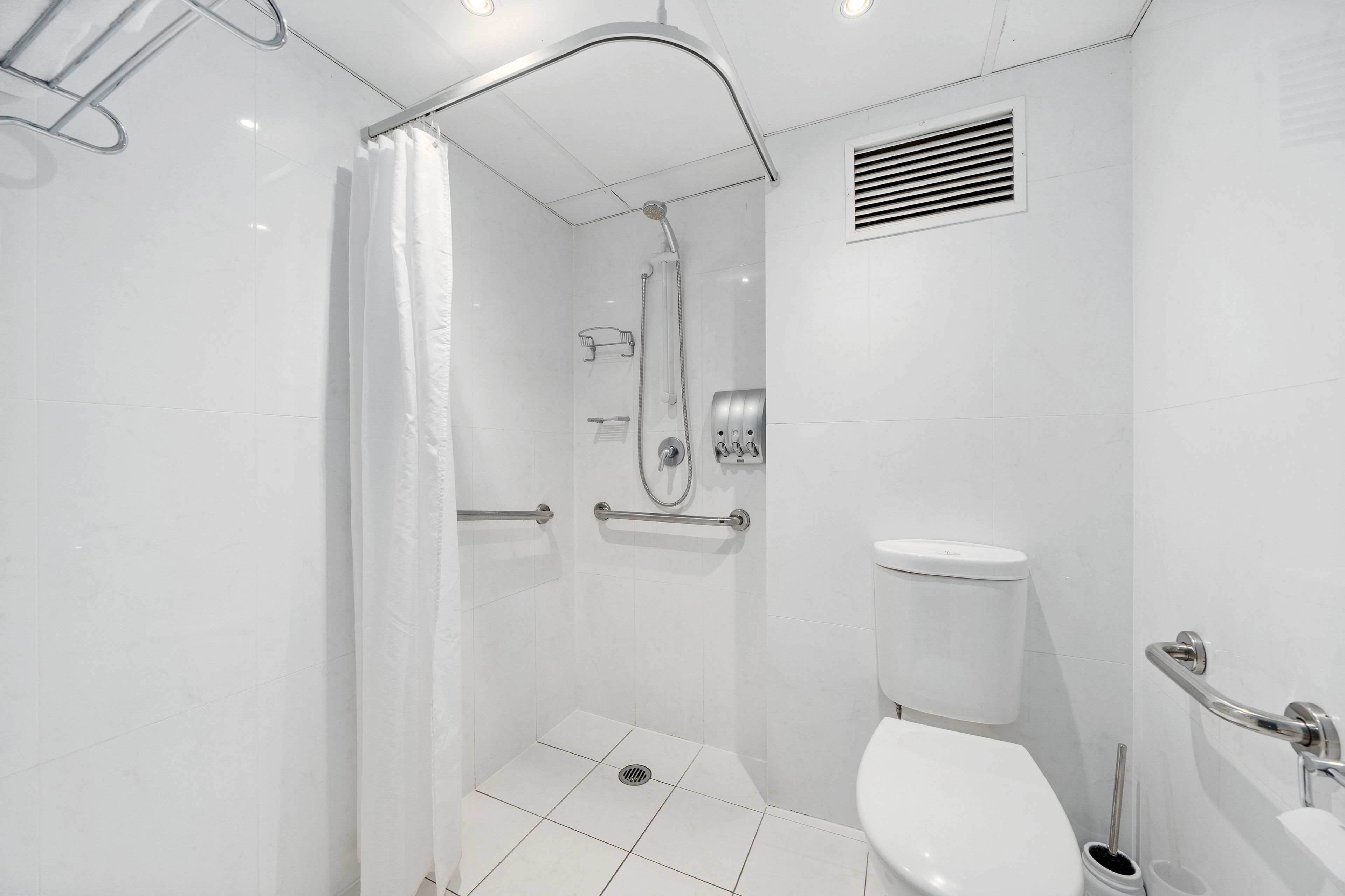 Un baño moderno con ducha a nivel, barras de apoyo, inodoro y secador de manos.
