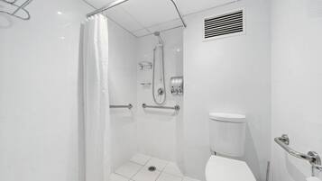 Un baño moderno con ducha a nivel, barras de apoyo, inodoro y secador de manos.