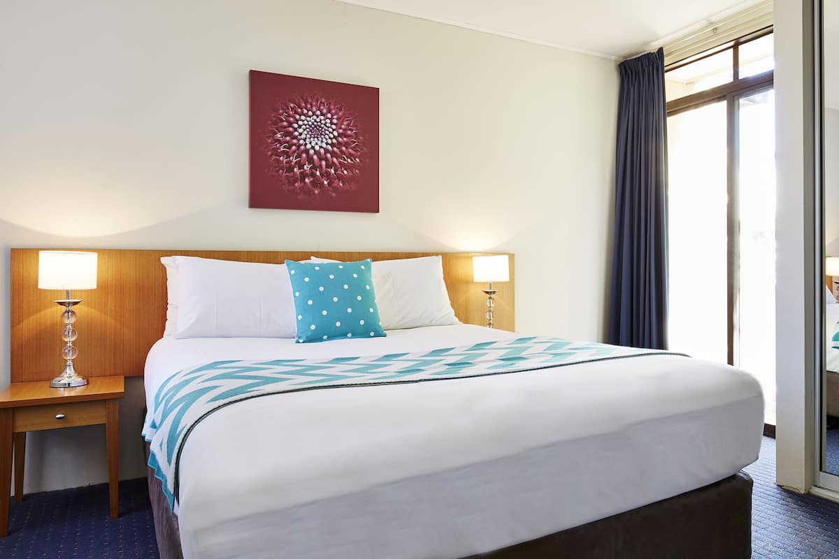 A hotel room with a large bed, two bedside tables with lamps, a mirror, and a wall art piece.