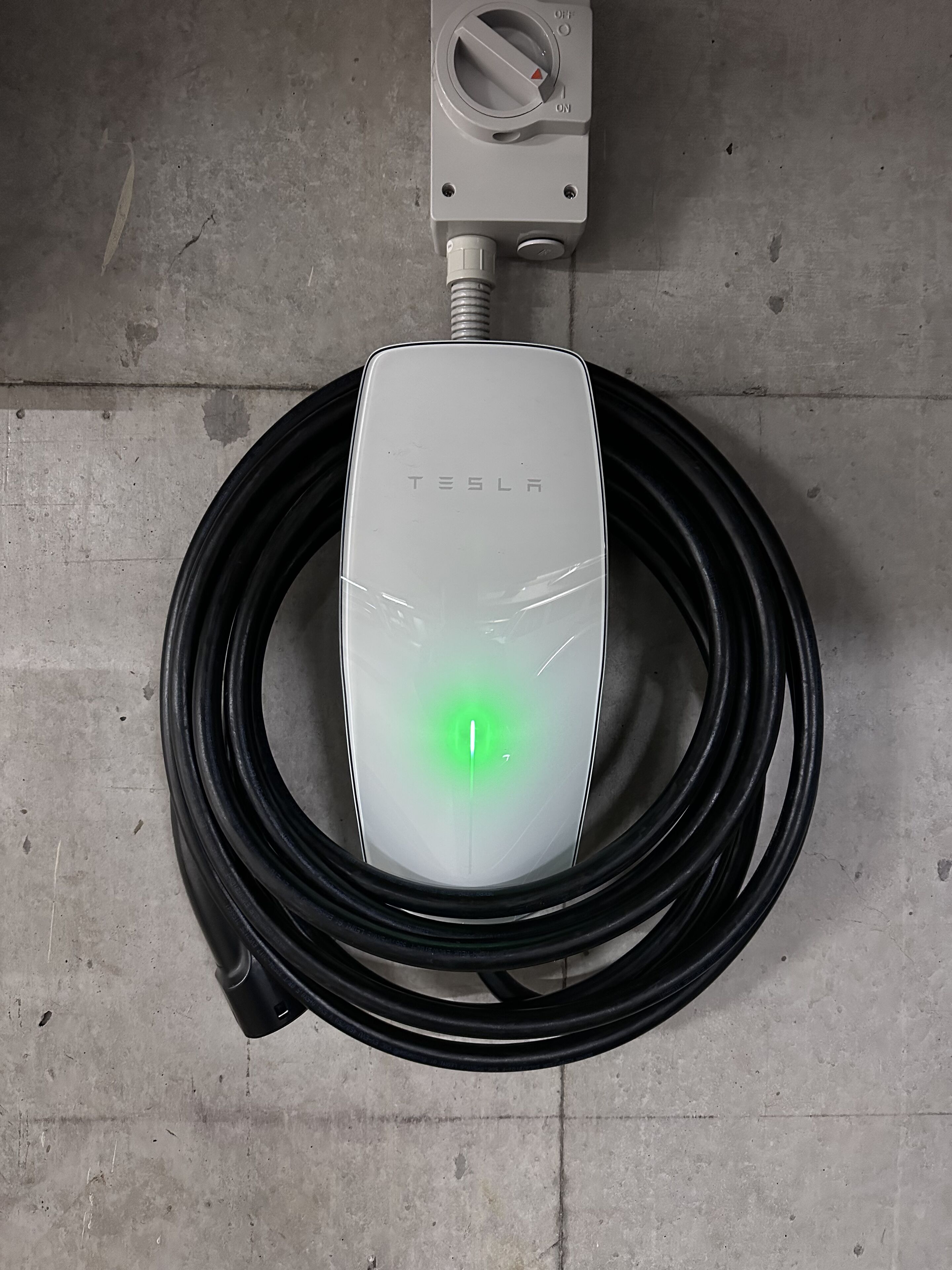 A Tesla charging station with a green light, a cable, and a control panel with an 'OFF' switch.