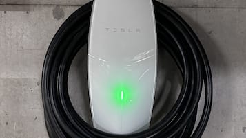 A Tesla charging station with a green light, a cable, and a control panel with an 'OFF' switch.