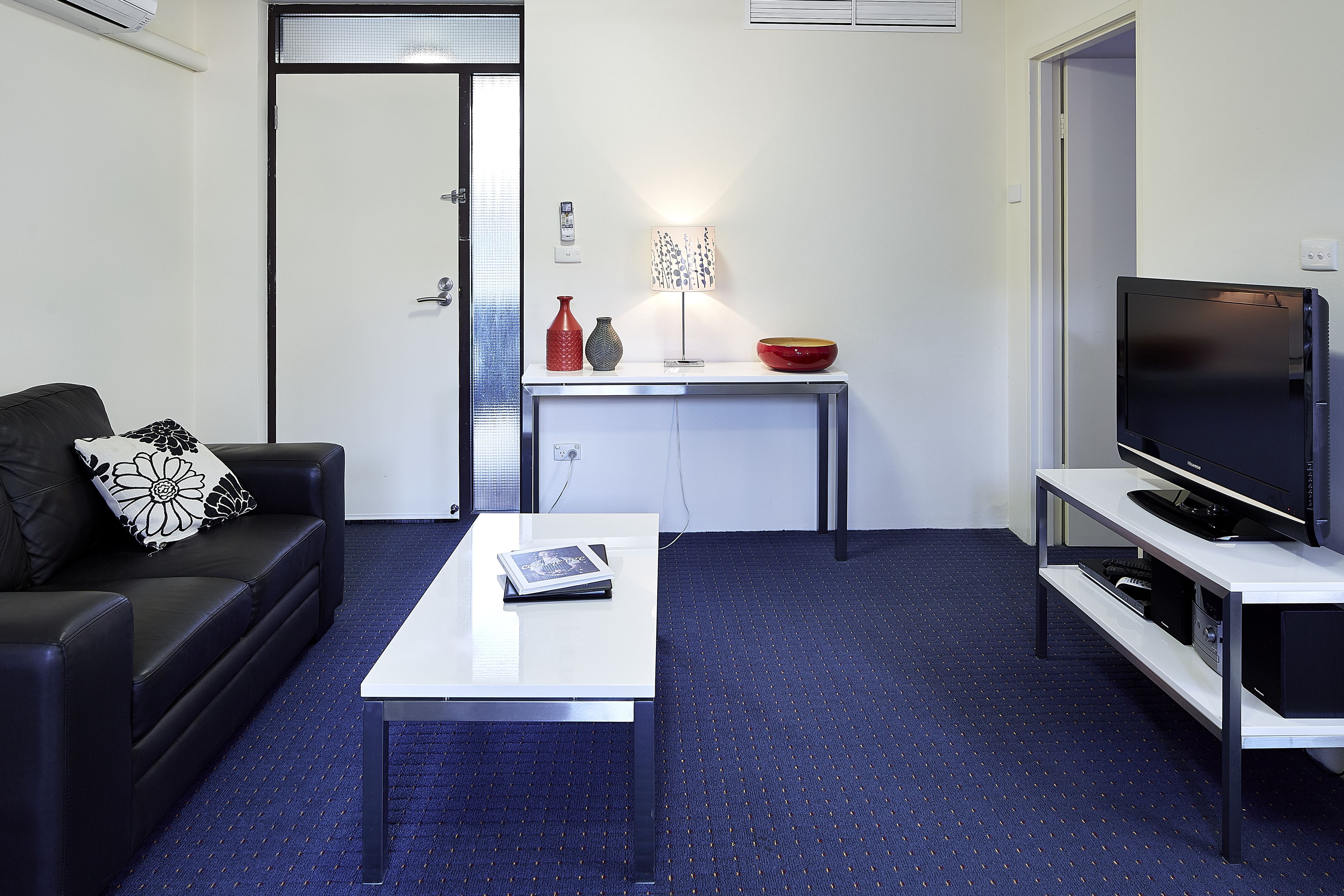 Een moderne woonkamer met een bank, salontafel, televisie en een klein tafeltje met decoratieve objecten.