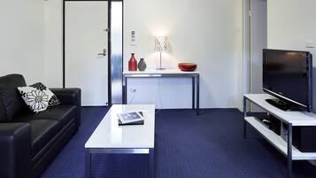 Een moderne woonkamer met een bank, salontafel, televisie en een klein tafeltje met decoratieve objecten.
