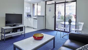 Una sala de estar moderna con un televisor de pantalla plana, un tazón rojo sobre una mesa blanca, un sofá de cuero negro y una mesa de centro de vidrio.