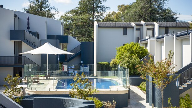 Un moderno edificio residencial con piscina, mobiliario exterior y una escalera que lleva a un balcón.