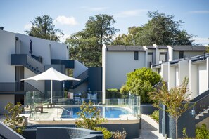 A modern residential building with a swimming pool, outdoor seating, and a staircase leading to a balcony. - Manuka Park Apartments (Griffith)